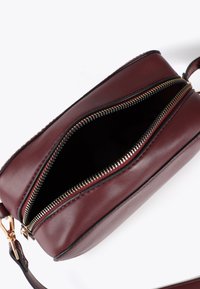 Borsa in pelle borgogna con due cerniere, parzialmente aperta, che rivela un interno scuro. Sono visibili dettagli in cerniera color oro e rifiniture nere.