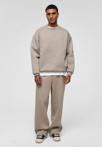 Beige sweater met drop shoulders en een losse pasvorm, gecombineerd met bijpassende wijde broek en donkere sneakers. Glad materiaal met minimale details.