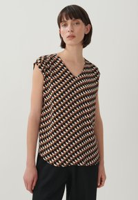 Korte mouwen blouse met V-hals, gemaakt van lichte stof. Het heeft een geometrisch patroon in bruin, zwart en crème kleuren.