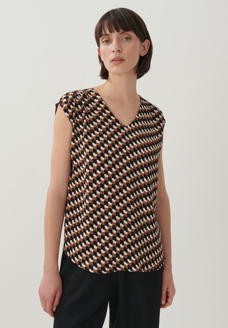 Korte mouwen blouse met V-hals, gemaakt van lichte stof. Het heeft een geometrisch patroon in bruin, zwart en crème kleuren.