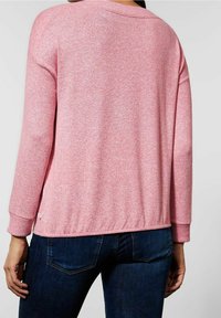 Różowy sweter z dzianiny o fakturze, z opuszczanymi ramionami, ściągaczami na mankietach i na dole. Charakteryzuje się lekko oversize'owym krojem i małą metką z logo.