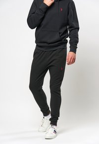 Svart huvtröja med röd logotyp, med en känguruficka och justerbar dragsko. Matchas med svarta smalare joggers i mjukt tyg.