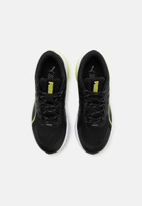 Baskets de sport noires avec tige en mesh, accents verts et semelle blanche. Présentent des lacets et le logo PUMA sur la languette.