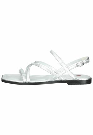Sølv flade sandaler med krydset stropper, lavet af et skinnende materiale, med en flad sort sål og en justerbar ankelrem.