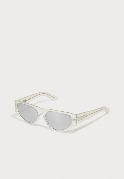 Sunglasses with a transparent frame, gray lenses, angular design, and narrow temples featuring a subtle logo accent.