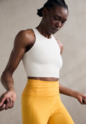 White cropped athletic tank top paired with high-waisted yellow leggings. Smooth fabric with a fitted design and minimal seams.