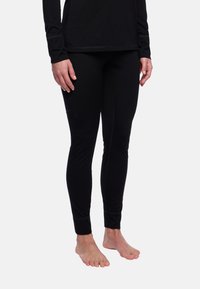 Leggings noirs ajustés en tissu lisse, avec une taille haute et des détails de couture subtils, associés à un long haut noir.