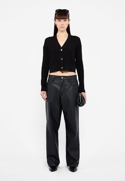 Black ribbed cardigan with gold buttons, paired with high-waisted black leather pants. Model holds a small black clutch, wearing sunglasses.