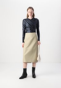 Langermet, marineblå satintopp med innviklet design, kombinert med kne-lengde, beige skjørt og svarte lær ankelstøvler. Holder en liten hvit veske.