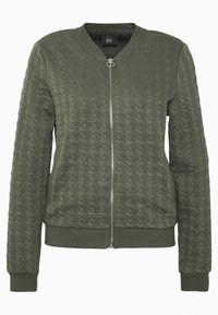 Olivgrön bomberjacka med quiltad textur, ribbade manschetter och nederkant, full dragkedja framtill och rund hals. Har en liten varumärkesskylt inuti.