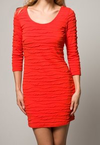 Červené šaty s kulatým výstřihem a tříčtvrtečními rukávy, s texturovaným, vlnitým vzorem po celé látce. Přiléhavý střih.