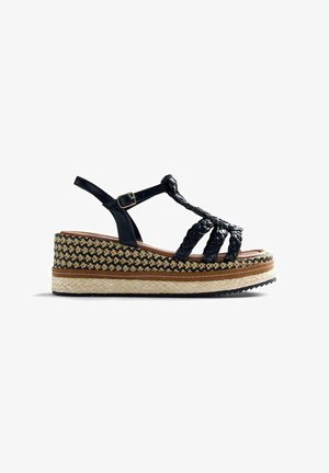 Sandale compensée à bride noire tressée avec boucle réglable, semelle intermédiaire à motif, et semelle plate-forme tressée de style espadrille.