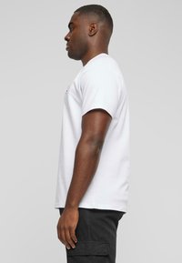 White cotton t-shirt with short sleeves, crew neck, and side view. Features a subtle logo on the chest and a relaxed fit.