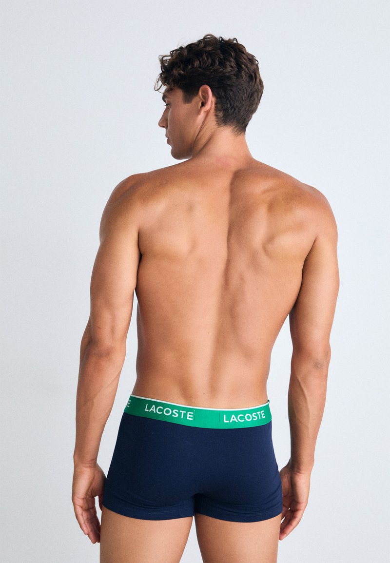 Shorts de bain bleu marine avec une ceinture élastique verte arborant le logo blanc "LACOSTE", fabriqués en tissu stretch lisse, design ajusté.