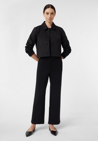 Zwarte cropped jas met een kraag en een knoopsluiting aan de voorkant, gecombineerd met hoge taille zwarte broek. Geweven stof, minimaal ontwerp.