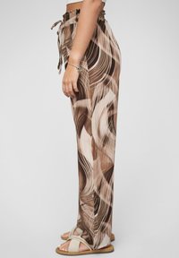 Wide-leg brown patterned pants featuring a soft, flowing fabric with abstract waves and a drawstring waist. Paired with light sandals.