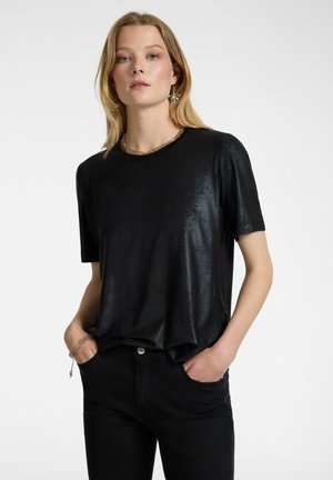 Top nero a maniche corte in materiale lucido, con scollatura rotonda e vestibilità ampia, abbinato a jeans denim scuri.