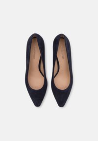 Navy blue suede pumps with pointed toe and cut-out design. Featuring a smooth, textured finish and a beige insole with logo.