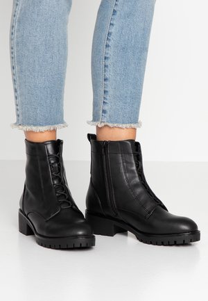 Bottines noires en cuir à lacets avec fermetures éclair latérales portées avec un jean bleu clair à ourlet effiloché.
