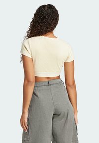 Kreemist lühikeste varrukatega lühikese lõikega t-särk, millel on ribakujuline tekstuur ja dekoratiivne sisekant sinise logo kujutisega, paaritatud hallide cargo-pükstega.