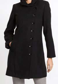 Svart ullkappa med hög krage, sju knappar framtill och två sidofickor. Slät textur med skräddarsydd silhuett.