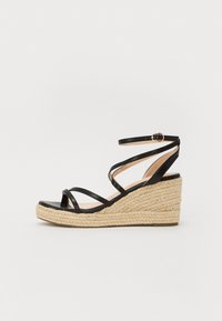 Mustad mustad sandaalid, millel on espadrille-stiilis köie alus, mitme rihmaga ja pahkluu pandlaga. Siledat tekstuuri ja avatud varvaste disain.