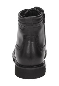 Stivaletto in pelle nera con dettagli brogue, zip laterale e suola in gomma spessa, mostrato da dietro su uno sfondo bianco.