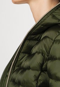 Olivengrøn pufferjakke med lynlås foran, der har quiltet design og hætte. Stoffet ser glat og let glansfuldt ud.