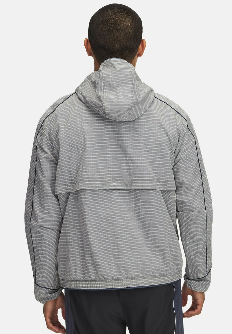 Veste légère à carreaux gris avec capuche, poignets élastiques et coupe loose. Présente des coutures noires contrastantes et un détail de ventilation à l'arrière.