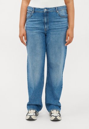 Forfra vy af en person iført lyseblå straight-leg jeans med falmede detaljer og hvide og sorte sneakers.