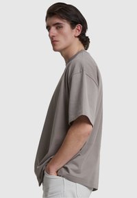 Tricou oversized de culoare gri deschis, dintr-un material moale, cu mâneci scurte, guler rotund și un croi lejer. Textură netedă și design minimal.