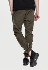 Pantalones cargo verde oliva con puños elásticos y múltiples bolsillos, combinados con zapatillas negras con suelas texturizadas y diseño slip-on.