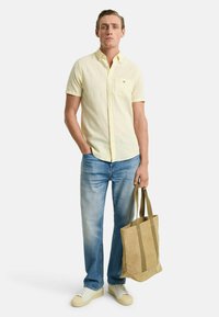 Camicetta gialla chiara a maniche corte con strisce bianche, jeans blu e una borsa a tracolla marrone con accenti verde scuro. Scarpe casual color avorio.