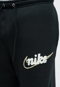 Melnas sporta bikses ar izšūtu baltu "nike" logotipu un bēša krāsas svītru. Materiāls ir gluds ar teksturētu virsmu. Aizdare ar auklu.