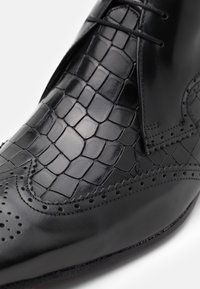 Zapatos de cuero negro con un patrón texturizado de cocodrilo, acabado suave, detalles de brogue y cierre de cordones.