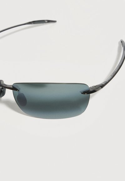 Ορθογώνια γυαλιά ηλίου με μαύρο πλαίσιο, σκούρους φακούς και λεπτούς βραχίονες σε απλό ανοιχτό φόντο.