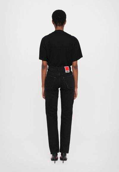 Black jeans with a fitted design, high waist, and red label at the back pocket. Paired with a loose black t-shirt and black heels.
