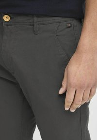 Donkergrijze chinos voor mannen, gemaakt van katoen met een gladde textuur. Beschikt over een gouden knoop en zijzakken, met een merketiket nabij de tailleband.