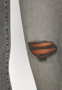 Jeans in denim grigio con ginocchio scolorito e diverse strappi orizzontali che lasciano intravedere la pelle. Vestibilità slim con texture liscia e lavaggio delicato.