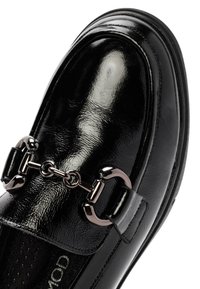 Zwarte lakleren loafers met een glanzende afwerking, een decoratieve ketting met hardwareaccenten en een rond uiteinde.