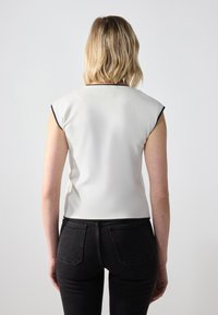 Kortermet, lysegrå topp med svart kant. Glatt tekstur, tettsittende design og rund halslinje, kombinert med svarte tettsittende jeans.