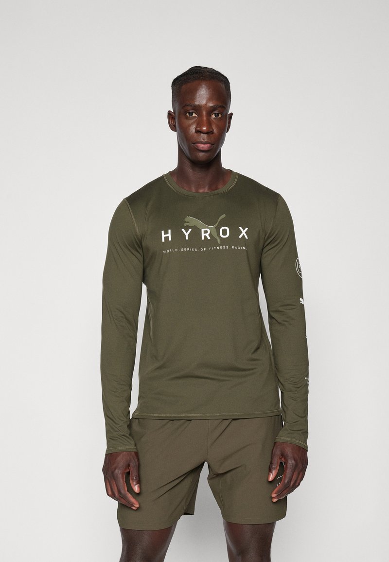 Olijfgroene sportshirt met lange mouwen en witte "HYROX" logo en tekst. Zachte stof, strakke pasvorm, met logo-accenten op de mouwen.