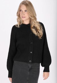 Zwarte gebreide cardigan met een geribbelde textuur, ronde halslijn en vijfknops sluiting. Heeft een verlengde schouderlijn en lange, iets puffed mouwen.