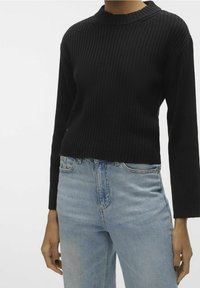 Maglione nero a coste con un col alto e maniche lunghe, abbinato a jeans in denim blu chiaro. Il maglione ha un design cropped.