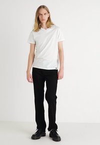 White cotton t-shirt with a v-neck design, paired with black straight-leg pants and black shoes. Simple, casual look.