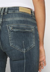 Tmavě modré denimové džíny s klasickým pětipocketovým designem, úzkou zadní kapsou a značkovou etiketou na pasu.