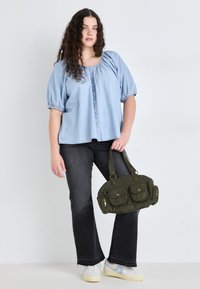 Lyseblå puffermet bluse med knapper, sorte flagrende jeans og en mørkegrønn corduroy håndveske med frontlommer og gulldetaljer.