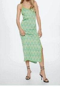 Robe midi à motif zigzag vert avec des bretelles fines, une fente sur le côté et une texture côtelée, associée à des sandales à talons hauts noires à lanières.