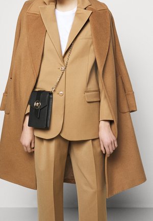 Beige vlněný oblek s dvouřadým sakem a širokými kalhotami. Nese se černá kožená crossbody kabelka se zlatým zapínáním.