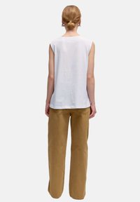 Top sans manches blanc avec un col rond associé à un pantalon ample taille haute beige. Matériau en coton, design simple, sans motifs visibles.